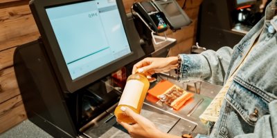 Zákaznice skenuje flašku džusu u samoobslužné pokladny.