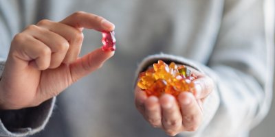 Žena drží v pravé ruce gumového medvídka v levé hrst bonbónů