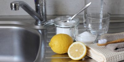 Rozpůlený citron, sklenička s jedlou sodou, kartáček a utěrky na odkapávači vedle dřezu