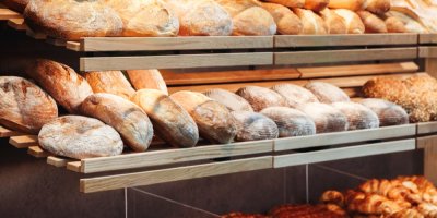 Bochníky chleba vyskládané na dřevěné polici v pekárně