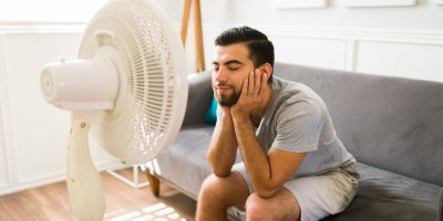 Muž sedí před ventilátorem v bytě