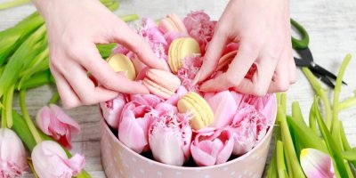 Žena urovnává do flower boxu s růžovými tulipány žluté a oranžové makronky.