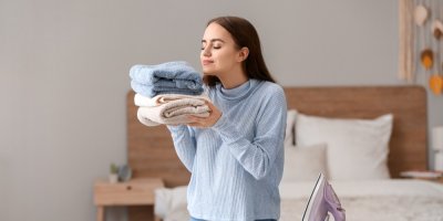 Mladá žena čichá k vyžehlenému prádlu, které drží v ruce