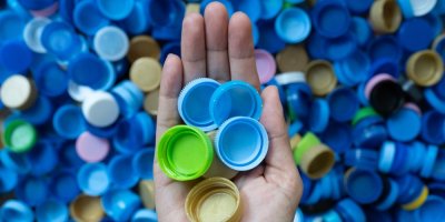 Ruka drží plastová víčka, v pozadí hromada víček různých barev