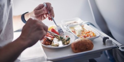 Muž jí v letadle příborem jídlo na bílém podnose.