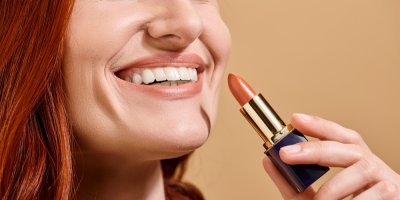 Žena se usmívá a drží v ruce rtěnku