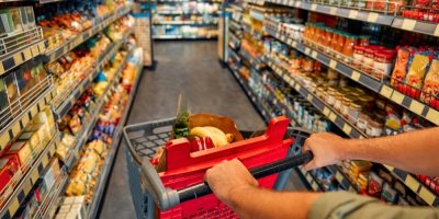 Muž tlačící nákupní vozík mezi plnými regály v obchodě