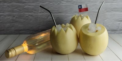 Láhev bílého vína ležící vedle tří žlutých melounů naplněných ledem a s brčky.