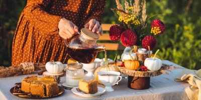Žena nalévá čaj venku, na stole je dort a dekorace