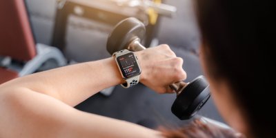 Muž se dívá  na chytré hodinky a drží v ruce činku