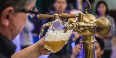 Muž čepuje do skleněného půllitru napěněné pivo z pípy.