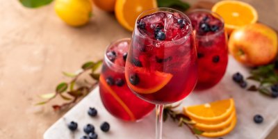 Sklenky míchaného drinku červené barvy s ledem, borůvkami a kousky pomeranče