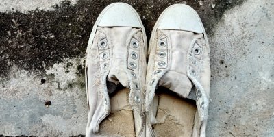 Záběr na špinavé a roztrhané béžové plátěné tenisky bez tkaniček