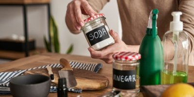 uce drží sklenici s jedlou sodou, na stole je položený ocet, citrony, prkénko, nůž a další kuchyňské potřeby