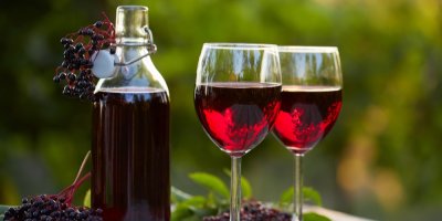 Lahev a dvě skleničky na víno naplněné červeným bezinkovým vínem.