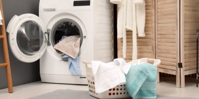 Otevřená pračka, ve které jsou ručníky, koš na prádlo s ručníky