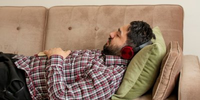 Muž spí na gauči se sluchátky na hlavě