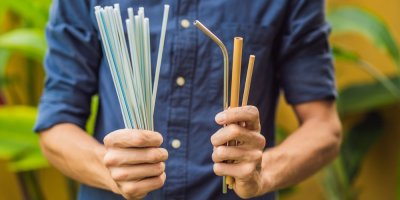 Muž drží v jedné ruce plastová brčka, v druhé jejich alternativy, kovové, papírové a jedlé brčko.