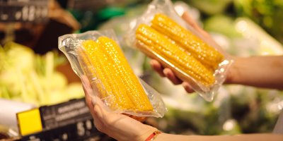 Člověk drží dva balíčky předvařené kukuřice v supermarketu.