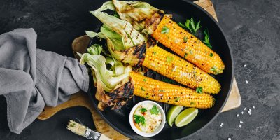 Tři grilované kukuřičné klasy na talíři, dip, limetka