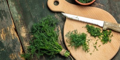 Pohled shora na prkénko s nožem a pokrájeným čerstvým koprem