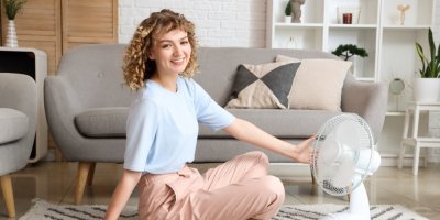 Žena se usmívá a má ruku položenou na stolním ventilátoru