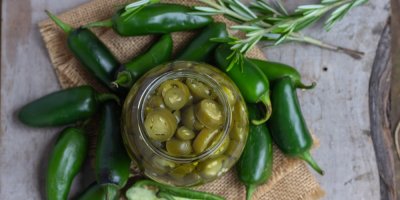 Zelené papričky naložené ve sklenici, kolem čerstvé papričky