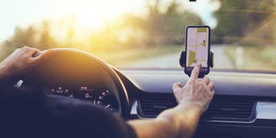 Řidič sedí za volantem a pravou rukou nastavuje GPS v telefonu, který je v držáku