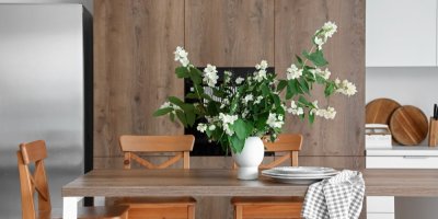 Váza s kvetoucím jasmínem uprostřed hnědého jídelního stolu, na kterém je položená utěrka a talíře