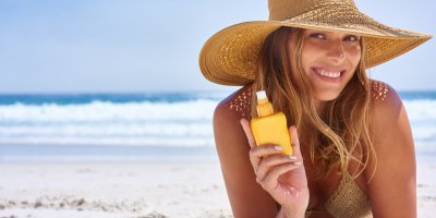 Žena s kloboukem u moře drží sprej