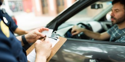 Policista vypisuje na papíru pokutu, v pozadí řidič za volantem