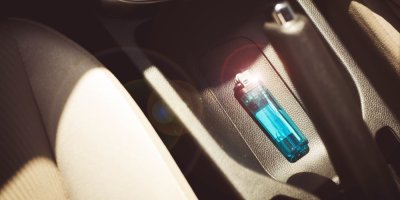 Průhledný zapalovač leží v autě na sedačce a svítí na něj slunce.
