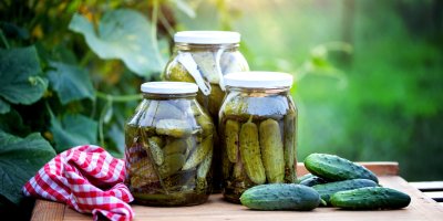 Sklenice naložených kyselých okurek, okurky a utěrka na dřevěném prkénku
