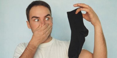 Muž drží v ruce černou ponožku a druhou rukou si zacpává nos