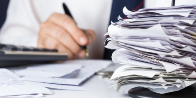 Stoh účtenek, v pozadí ruka držící propisku