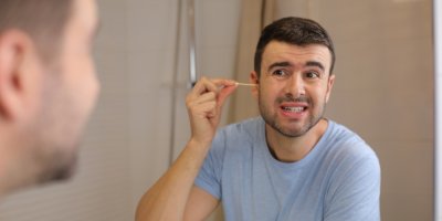 Muž si před zrcadlem čistí uši vatovou tyčinkou.