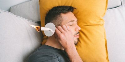 Muž leží na gauči a v uchu mu hoří ušní svíce.