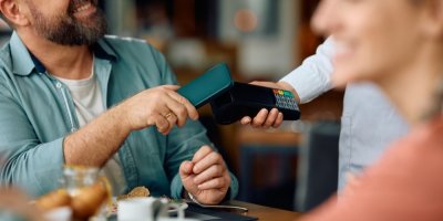 Muž platí bezkontaktně pomocí přiložení telefonu k platebnímu terminálu.