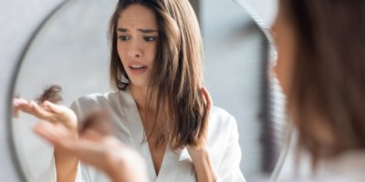 Žena drží v dlani chumáč vlasů a znepokojeně si ho prohlíží