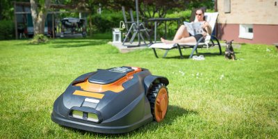 Žena se opaluje v zahradě s robotickou sekačkou