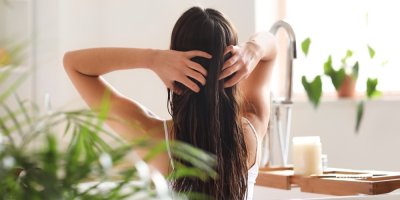 Žena v koupelně si upravuje vlhké vlasy.