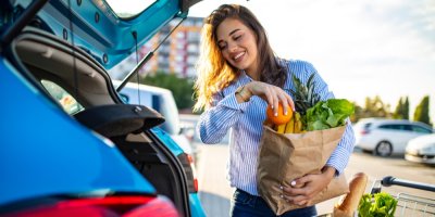 Žena nakládá nákup v papírových taškách do kufru auta.