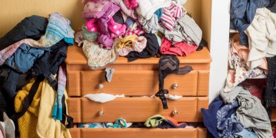 Prádelník přeplněný oblečením, které je poházené i všude okolo něj.