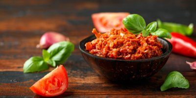 Rajčatové pesto v misce, kolem nakrájená rajčata a listy bazalky