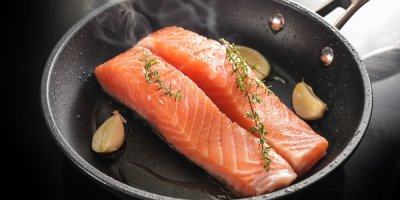 Filety lososa opékající se na pánvi se stroužky česneku