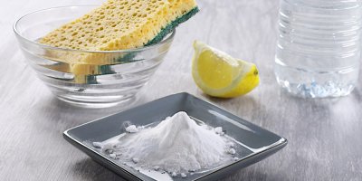 Bílý prášek na šedém talířku, vedle hubka na nádobí a citron s vodou