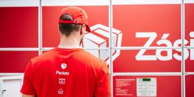 Doručovatel Zásilkovny v červeném oblečení stojí před Z-BOXem.