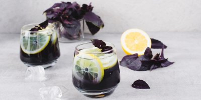 Skleničky s tmavým nápojem, kolečky citronu, ledem a lístky tmavé bazalky