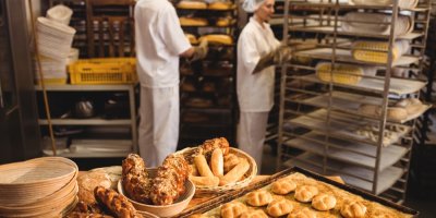 Čerstvě napečené pečivo a v pozadí pracovníci pekárny v pracovních úborech