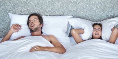 Žena si přikrývá uši polštářem, vedle chrápe muž
